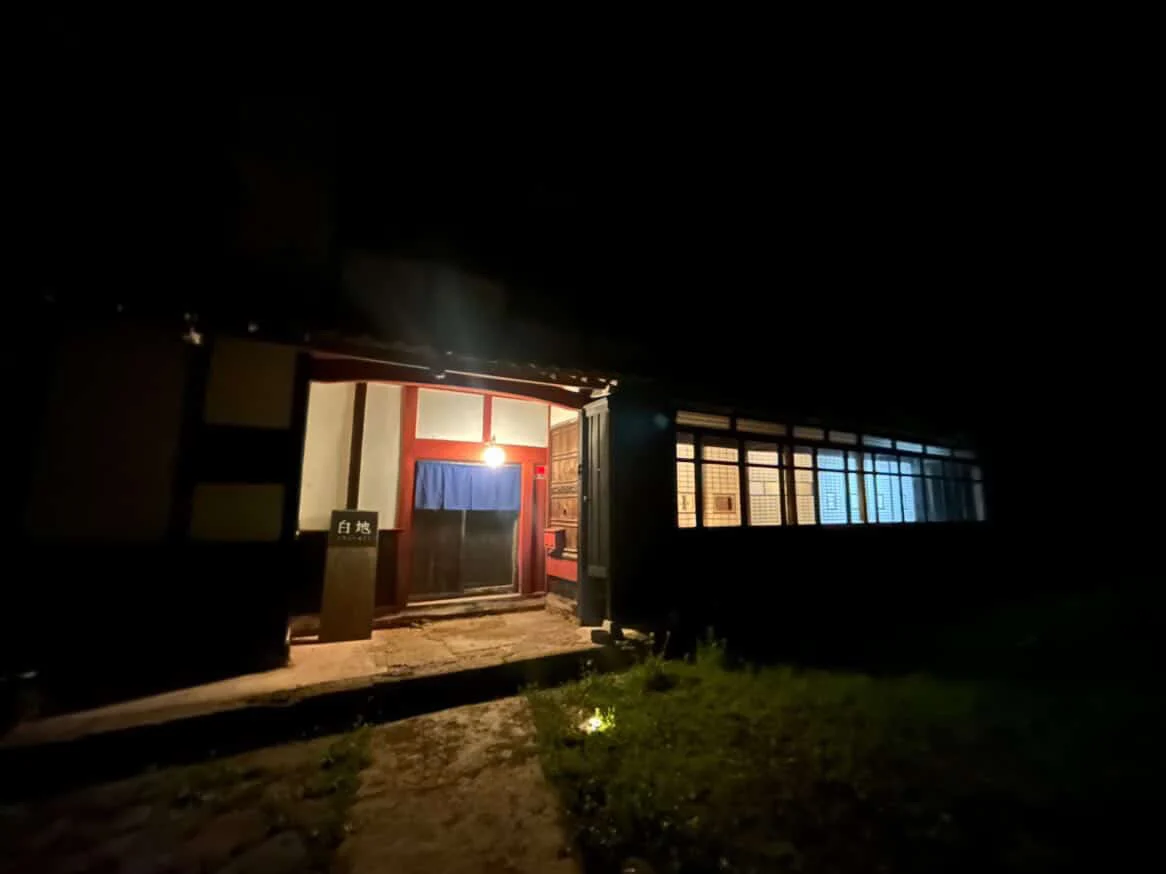 静かな夜に、玄関と窓の灯りが浮かび上がる白地